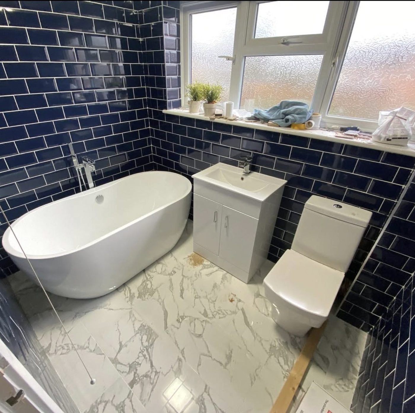 Navy metro tiled bathroom with a freestanding bath and marble effect floor